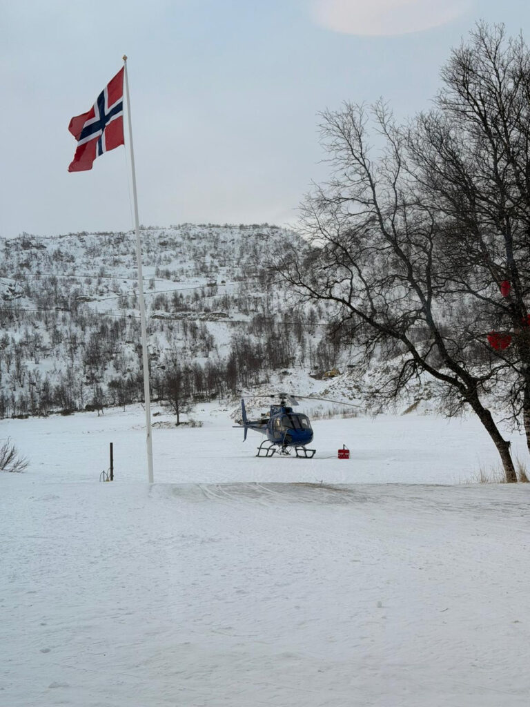 Bilde av et helikopter som står på snøen med den norske flagget foran