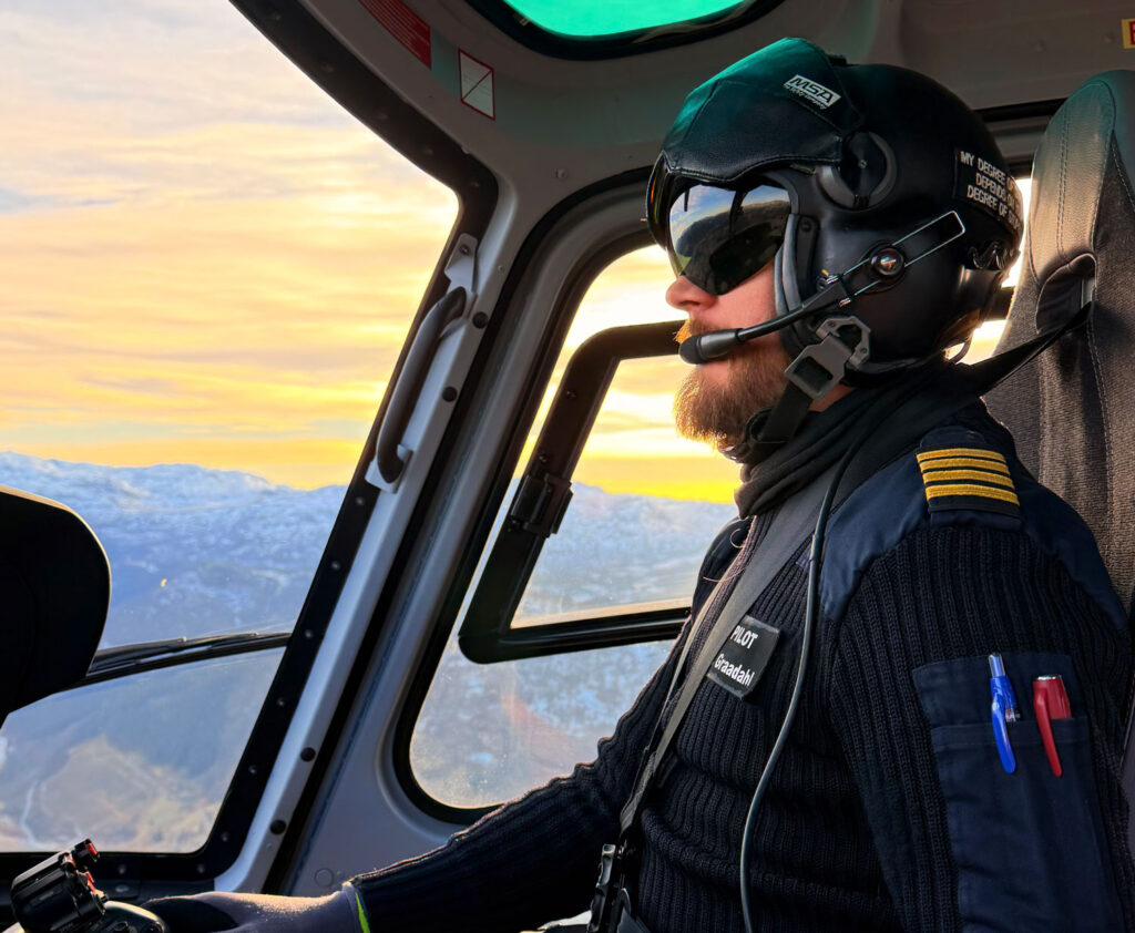 Bilde av en helikopterpilot som flyr i solnedgangen