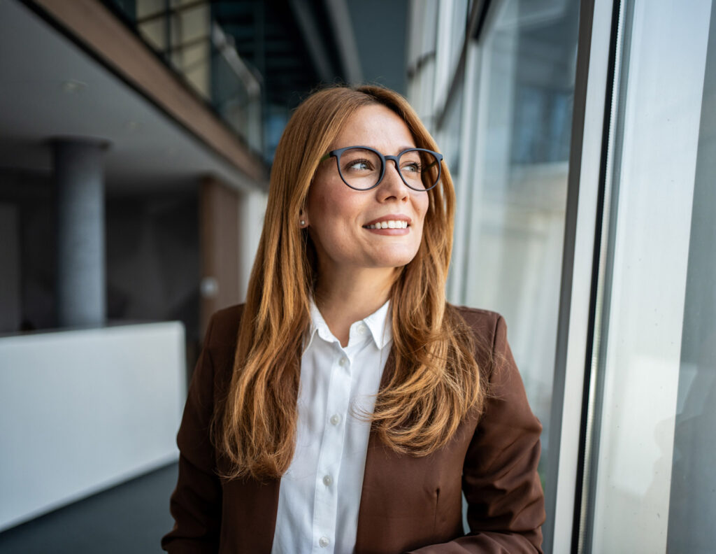 Bilde av en kvinne med rødt hår og briller som ser ut av et vindu