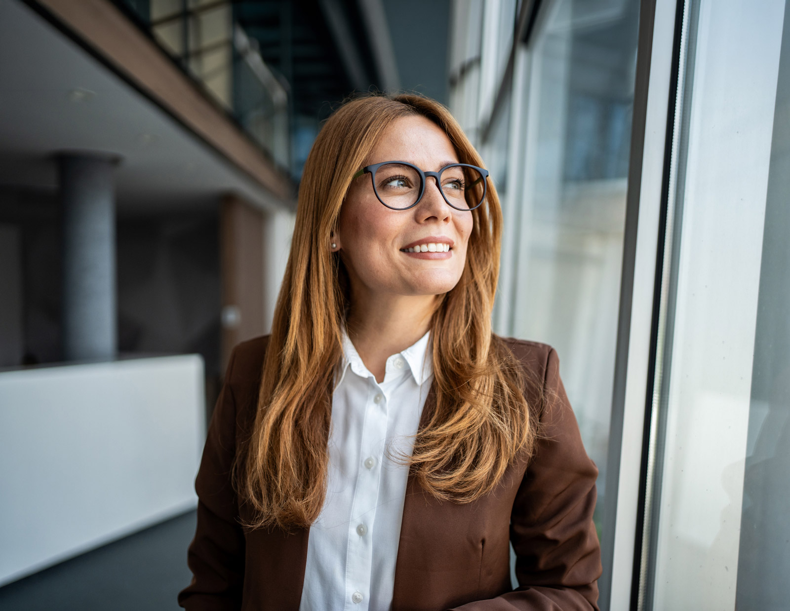 Bilde av en kvinne med rødt hår og briller som ser ut av et vindu